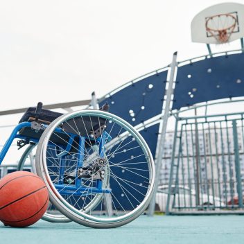 Image of empty wheelchair with basketball ball on the outdoor sport ground